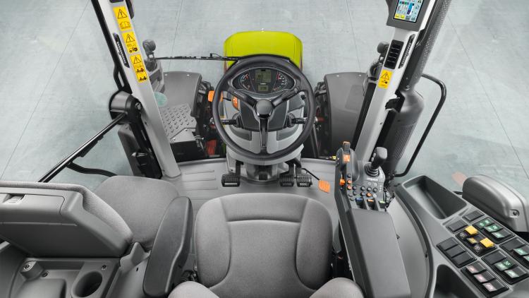 A kép egy traktor vezetőfülkéjének belső terét mutatja, a vezetőülésre, a kormánykerékre és a kezelőszervekre fókuszálva. A kép egy traktor vezetőfülkéjének belső terét mutatja, a vezetőülésre, a kormánykerékre és a kezelőszervekre fókuszálva.
