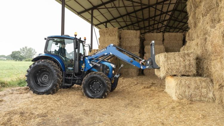 Egy kék Landini traktor látható egy pajtában, szalmabálák mellett.