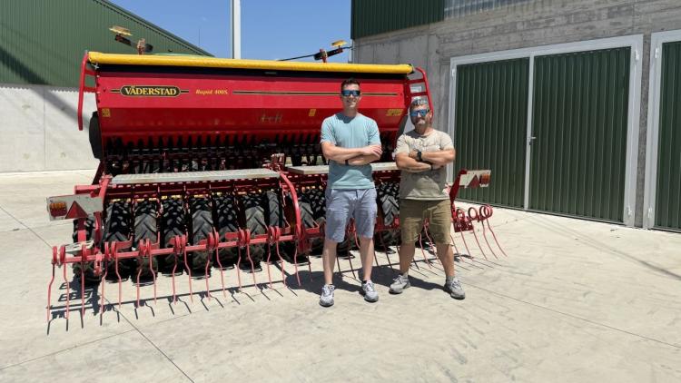 Két férfi áll egy nagy piros mezőgazdasági gép előtt egy farm udvarán. Két férfi áll egy nagy piros mezőgazdasági gép előtt egy farm udvarán.